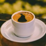 Steaming cup of black coffee placed on a saucer with blurred background.